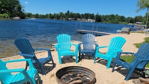 Eine Uferlage mit türkisblauen Adirondack-Stühlen, die um eine Feuerstelle im Sand angeordnet sind.