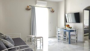 A modern hotel room with a bed, a desk with chairs, a flat-screen TV, and a large window with curtains. - Emorfia's Apartments No5 - 300m to the beach (Rethymno)