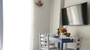 A dining area with a table, chairs, a flat-screen TV, and a wall-mounted air conditioner. - Emorfia's Apartments No5 - 300m to the beach (Rethymno)