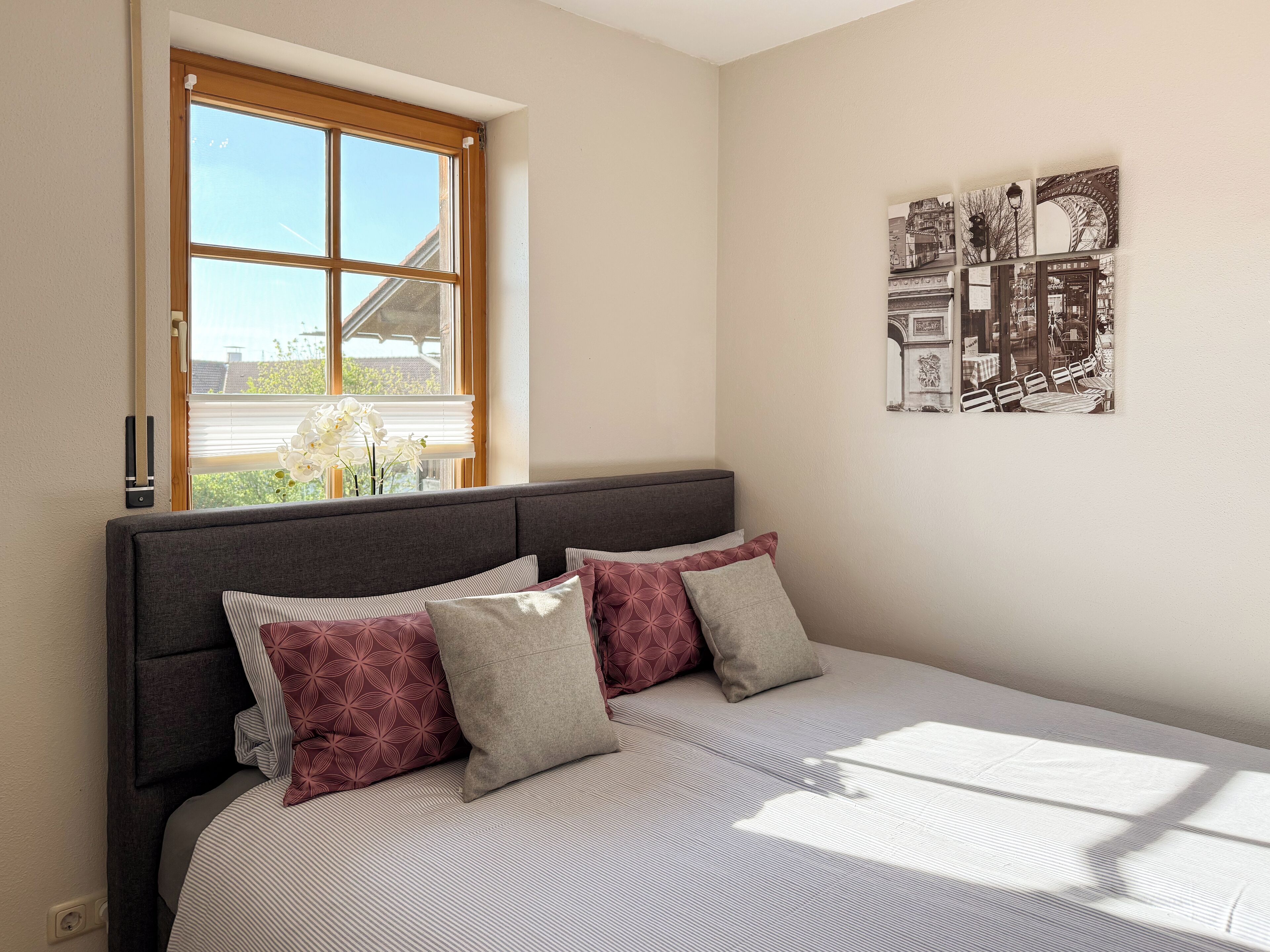 Un dormitorio con un ventanal grande, una cama con ropa de cama estampada y una obra de arte colgada en la pared.