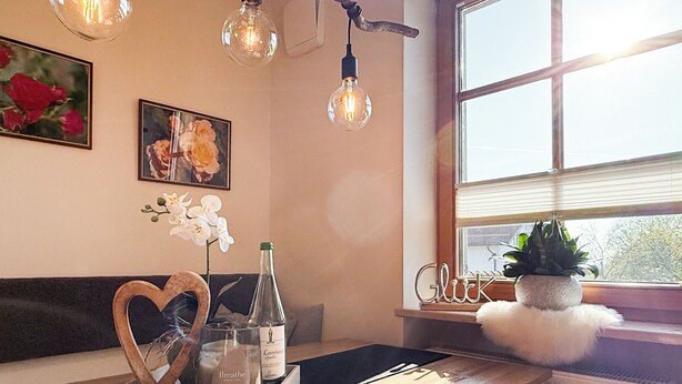 A cozy seating area with a wooden bench, a tray with candles and a bottle, and a window with a view. - Apartment Wohlfühlplatzl - Urgemütlich & Ruhig (Vogtareuth)