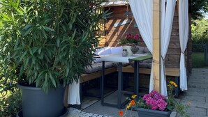 A wooden pergola with white curtains, a seating area with cushions, and potted plants. - Apartment Wohlfühlplatzl - Urgemütlich & Ruhig (Vogtareuth)