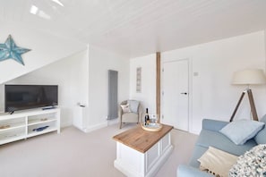 A modern living room with a flat-screen TV, a wooden coffee table, a blue sofa, and a star decoration on the ceiling. - Host & Stay | The Nest (Whitby)