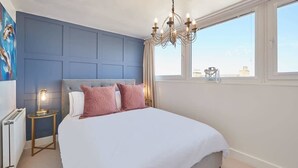 A bedroom with a large bed, a chandelier, a radiator, and a window with a view. - Host & Stay | The Nest (Whitby)