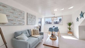 A modern living room with a light blue sofa, a wooden coffee table, and a city view through large windows. - Host & Stay | The Nest (Whitby)