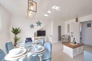 A dining area with a glass table set for six, a television in the background, and decorative stars on the wall. - Host & Stay | The Nest (Whitby)