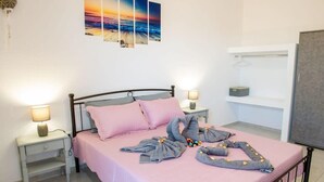 Ein ordentlich bezogenes Bett mit rosa Bettwäsche und dekorativen Handtüchern, ein Nachttisch mit Lampe und eine Wand mit einem Sonnenuntergangsgemälde.