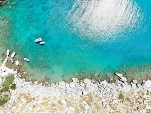 An aerial view of a coastal area with clear turquoise waters, rocky shoreline, and boats.