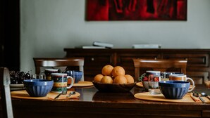 A dining table with a bowl of oranges, blue and yellow mugs, and a red abstract painting on the wall.