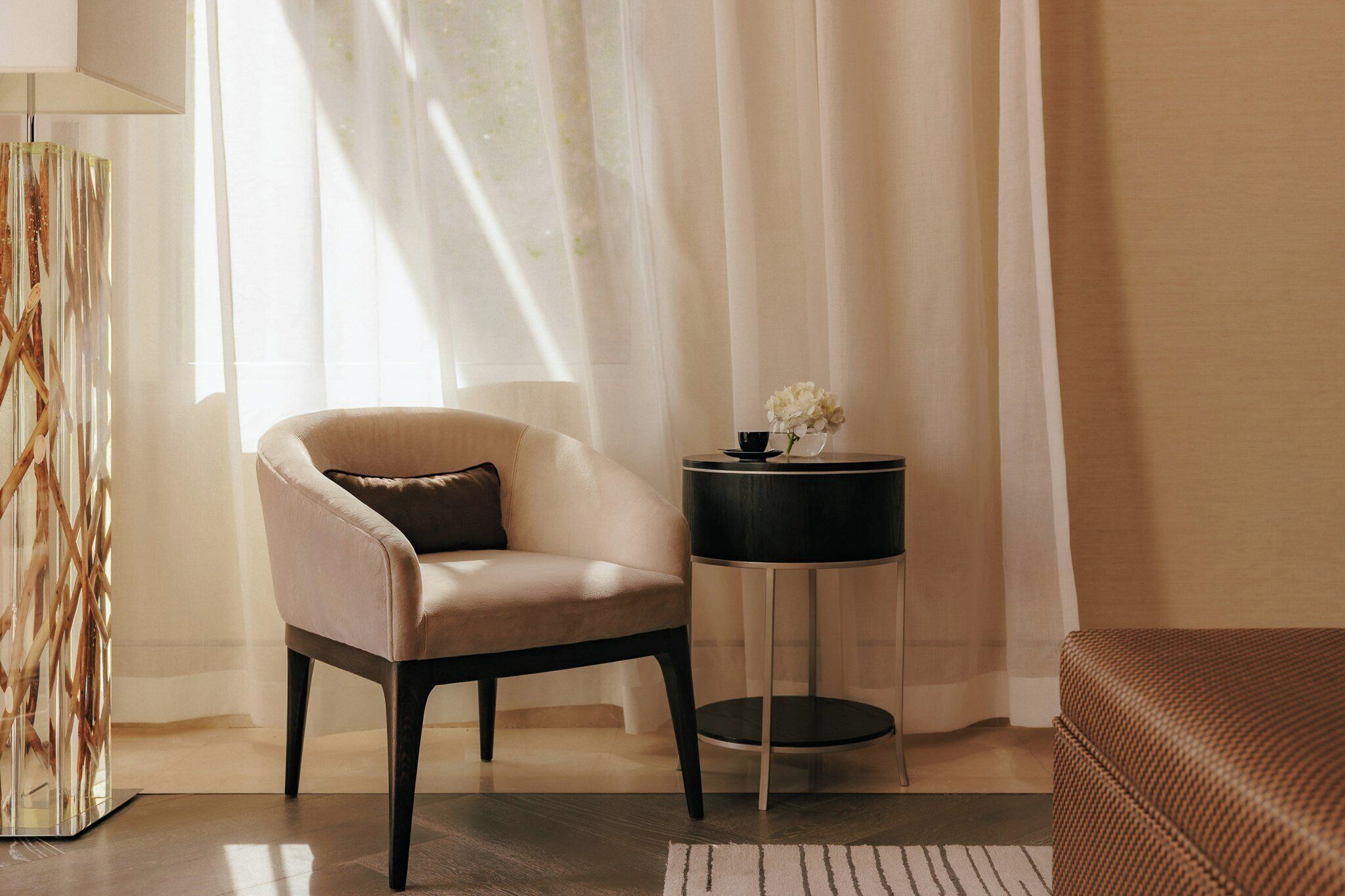 A room with a chair, a small table with a vase, and a lamp.