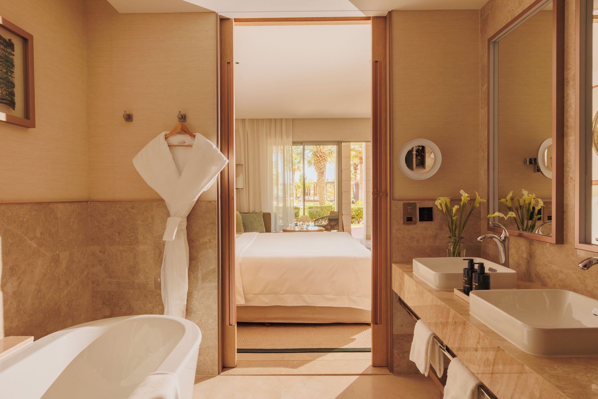 A modern hotel bathroom with a large bathtub, two sinks, and a walk-in shower.