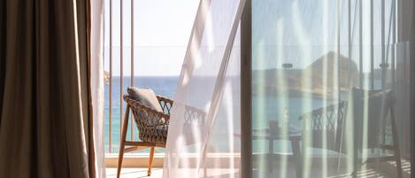 A room with a view of the sea, a wicker chair, and sheer curtains.