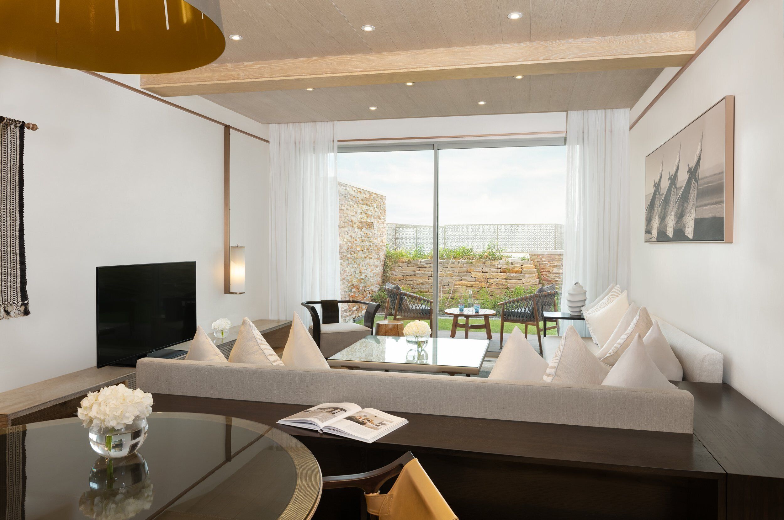 A modern living room with a sofa, a glass coffee table, a TV, and a view of the outdoor patio.