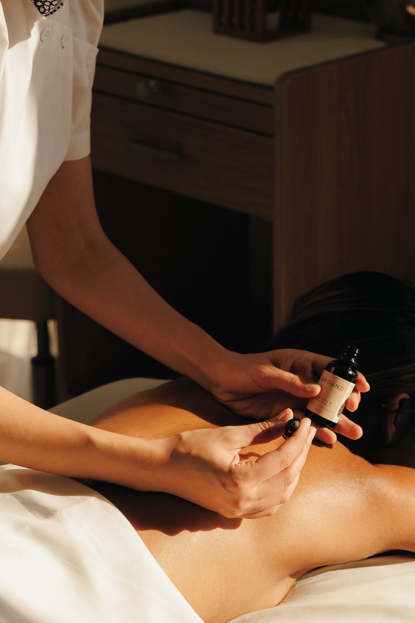 Une personne reçoit un massage, et une bouteille portant l'étiquette « GROUND » est placée sur son dos.