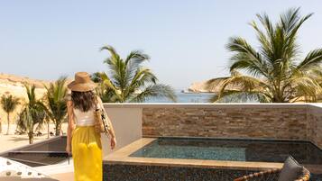 Zona de piscina con vista al mar, palmeras y una silla.
