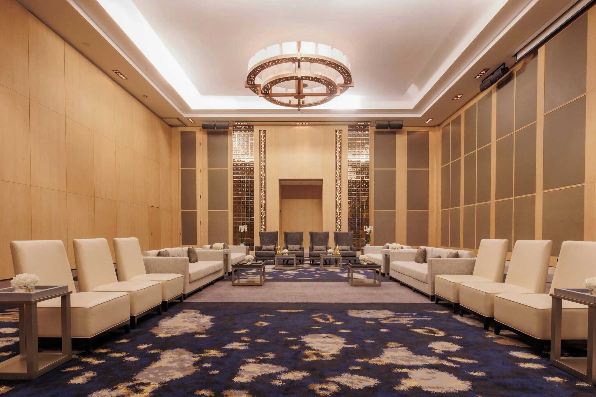 A hotel lobby with a central seating area, a chandelier, and a patterned carpet.