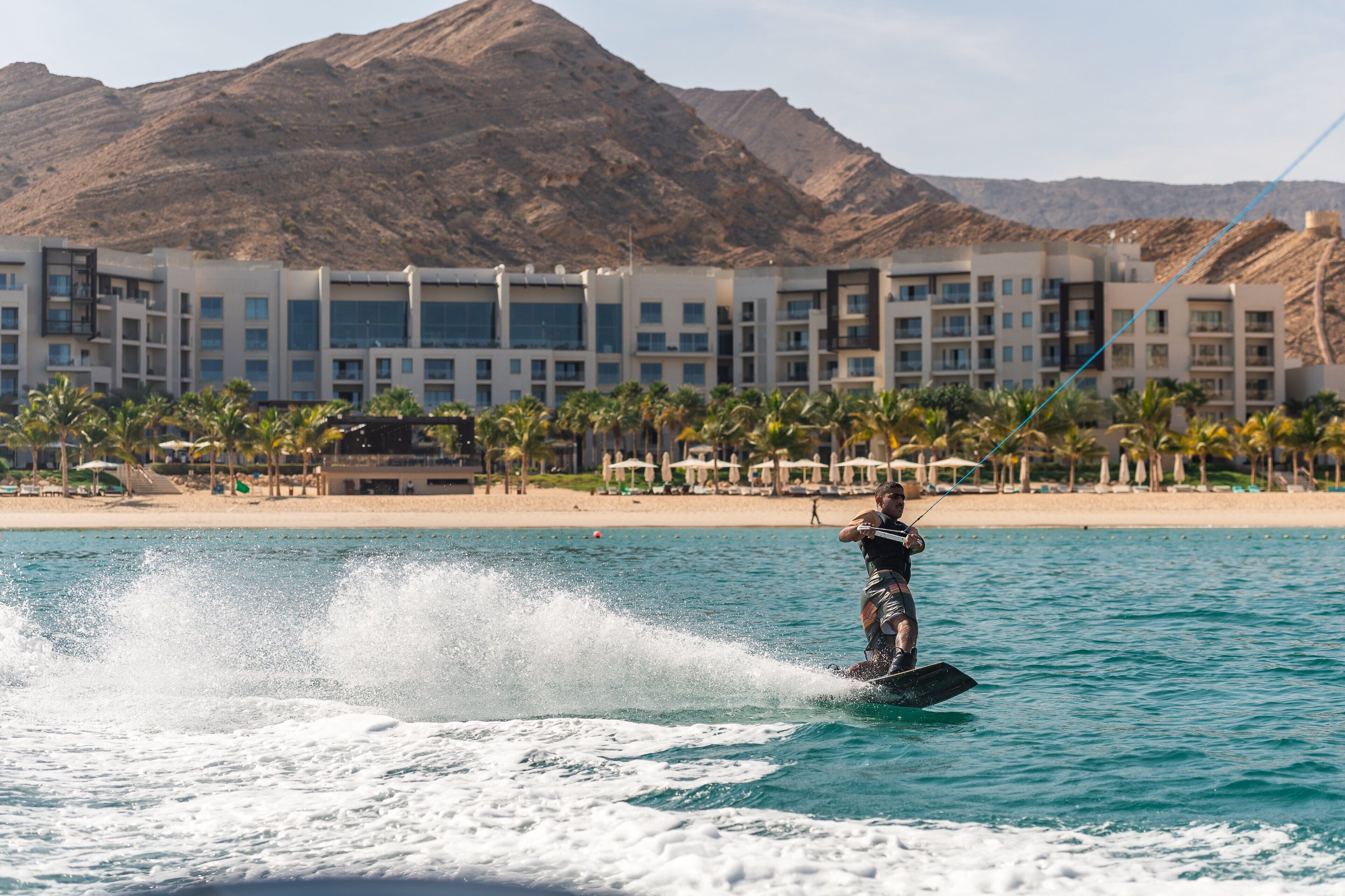 A person wakeboarding on a body of water with a resort in the background.