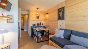 Une pièce chaleureuse avec un mur en bois, un canapé, une table avec des chaises et un téléviseur fixé au mur.