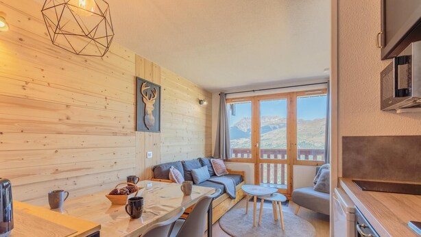 L’intérieur chaleureux d’un chalet avec un mur en bois, une table à manger avec des chaises, un canapé et un coin cuisine.