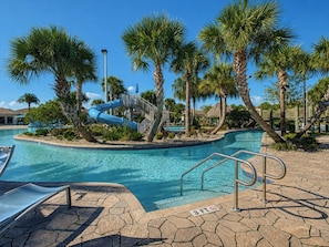 A swimming pool with a water slide, palm trees, and a lifeguard stand.
