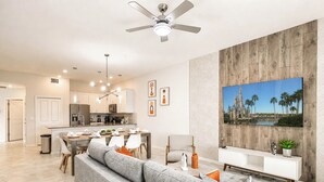 Ein modernes Wohnzimmer mit grauem Sofa, einem Essbereich mit Holztisch und einer Küche im Hintergrund.