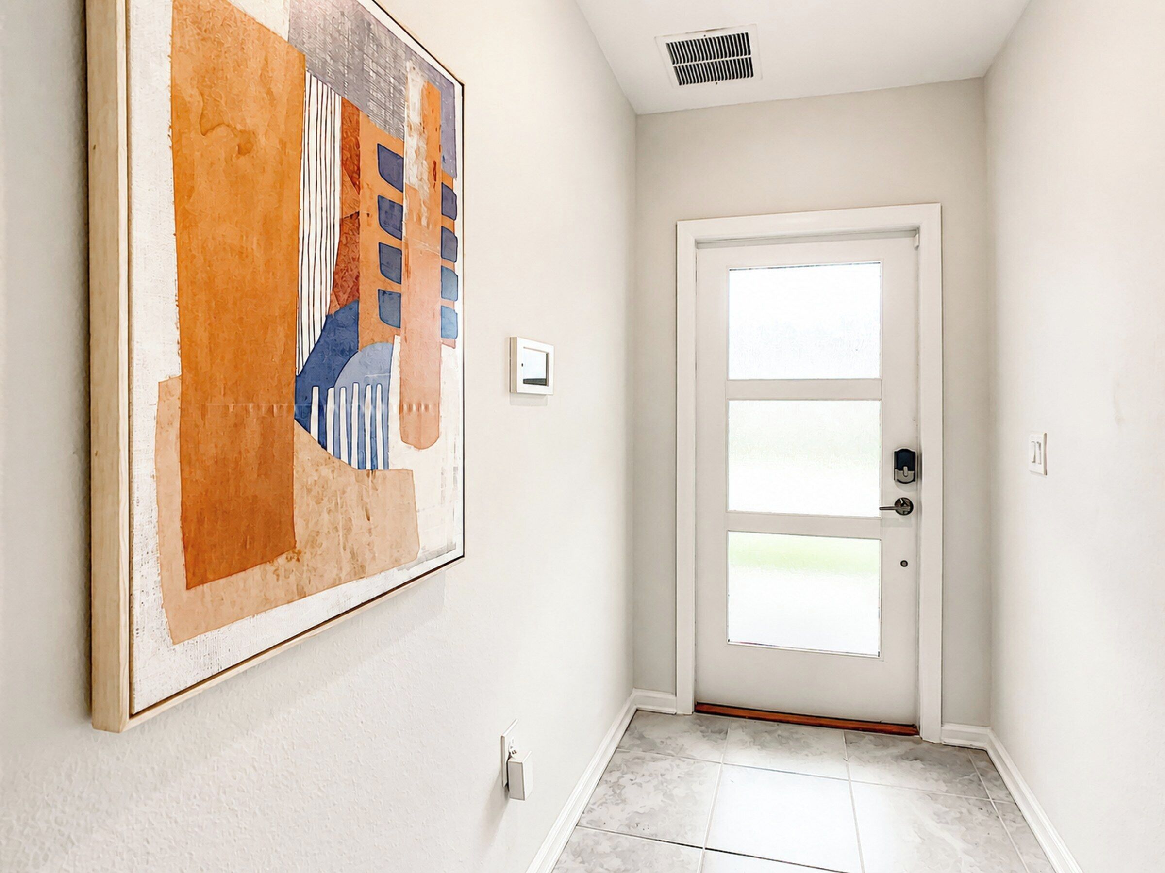 Un couloir avec une porte blanche, un interrupteur fixé au mur et un grand tableau abstrait.