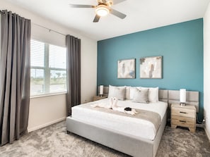 A bedroom with a bed, two bedside tables, a ceiling fan, and a window with curtains.