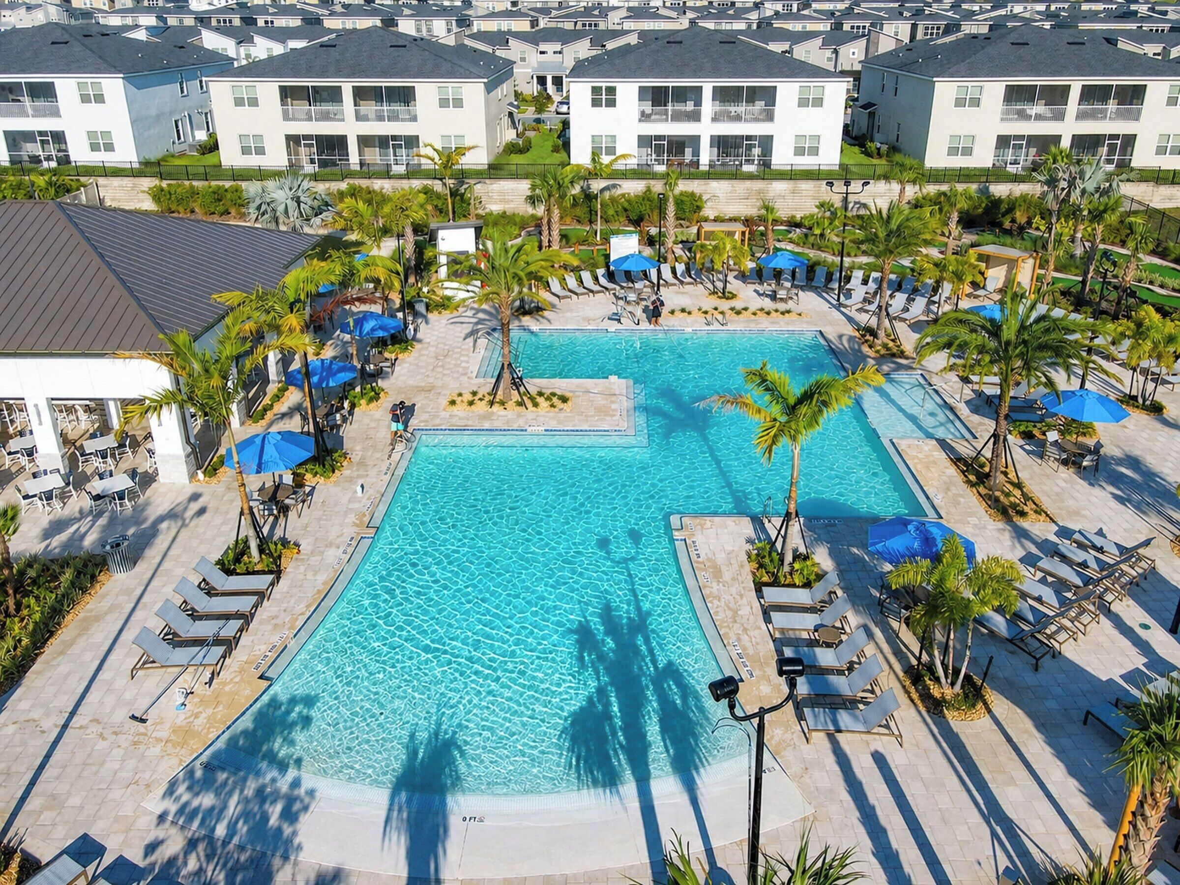 Ett semesterhotell med en central pool omgiven av solstolar och palmer.