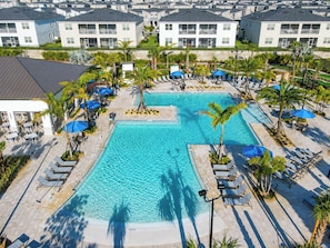 A resort with a central swimming pool surrounded by lounge chairs and palm trees.