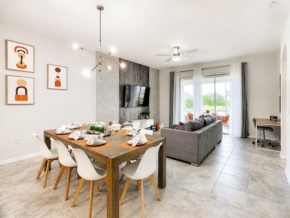 A modern dining area with a wooden table, white chairs, and a ceiling fan.