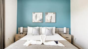 Une chambre d’hôtel avec un grand lit, deux tables de chevet, un mur d’accent bleu et des œuvres d’art abstraites.