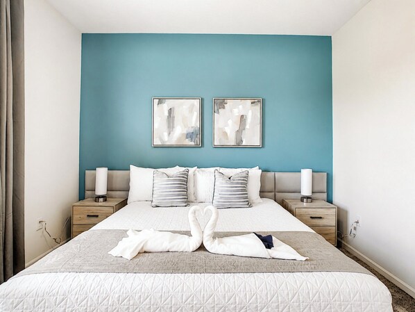A hotel room with a large bed, two bedside tables, a blue accent wall, and abstract art.