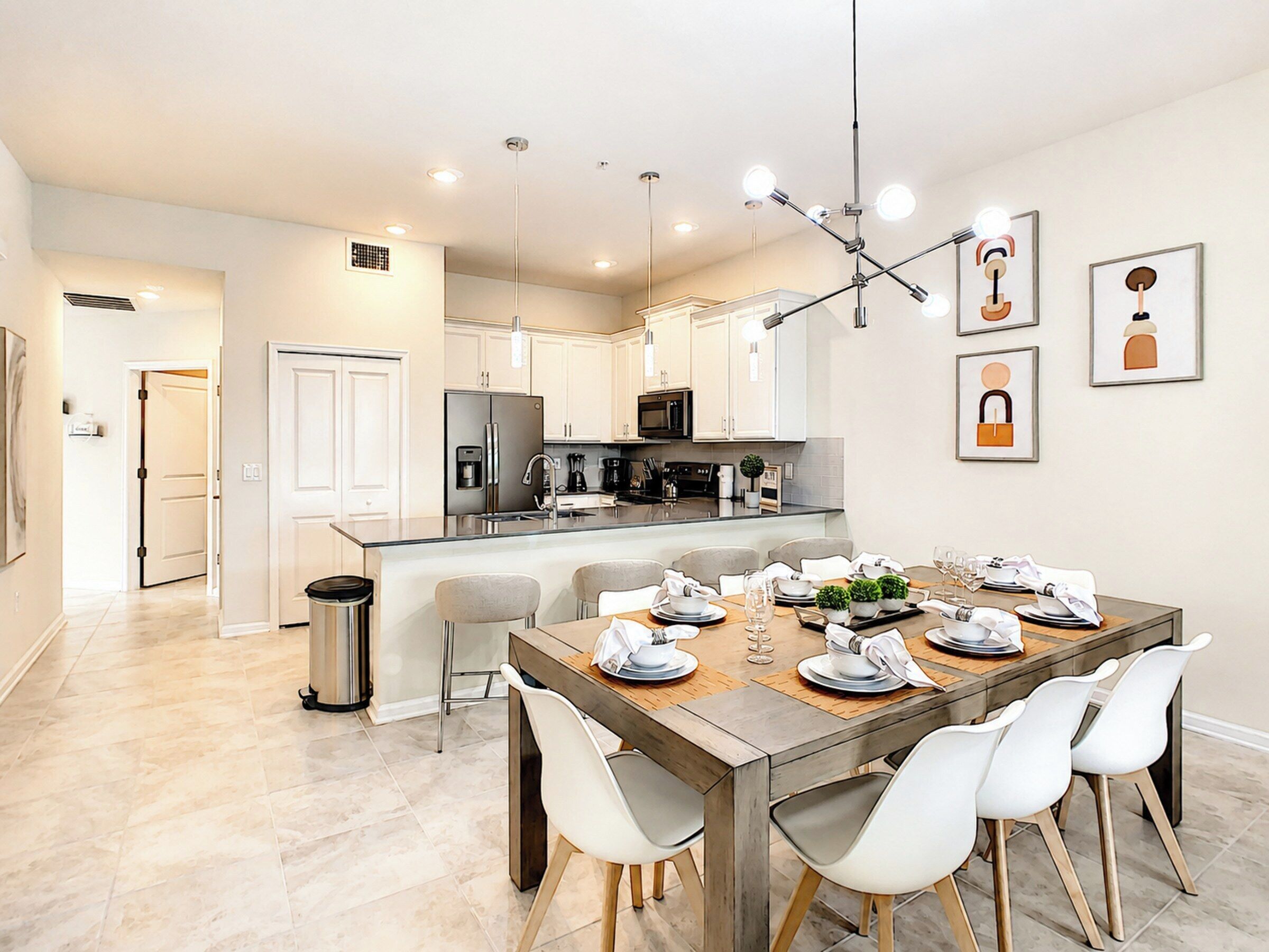 A modern kitchen with a central island, stainless steel appliances, and a dining area with a wooden table and white chairs.