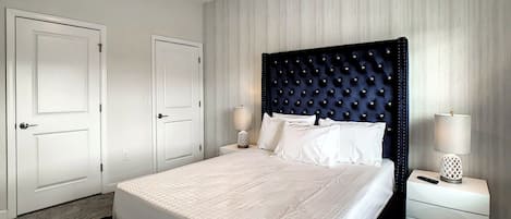 Un dormitorio con una cama grande, dos mesitas de noche, un ventilador de techo y una puerta.