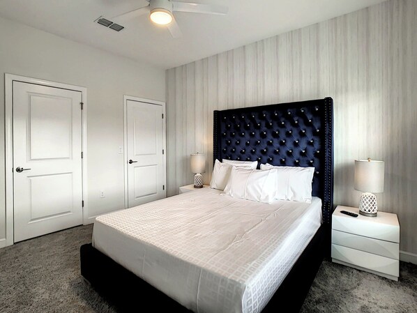 A bedroom with a large bed, two bedside tables, a ceiling fan, and a door.