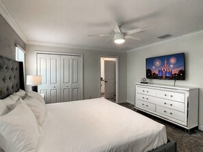 A bedroom with a bed, a dresser, a ceiling fan, and a wall-mounted TV.