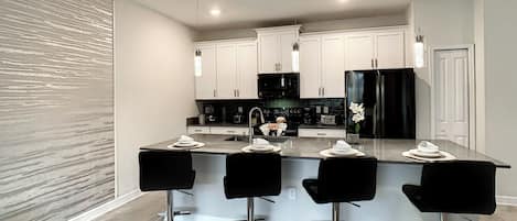 Una cocina moderna con armarios blancos, un refrigerador negro y una isla central con taburetes de bar.