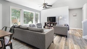 Ein modernes Wohnzimmer mit Sofa, Sessel, Esstisch und Fernseher.