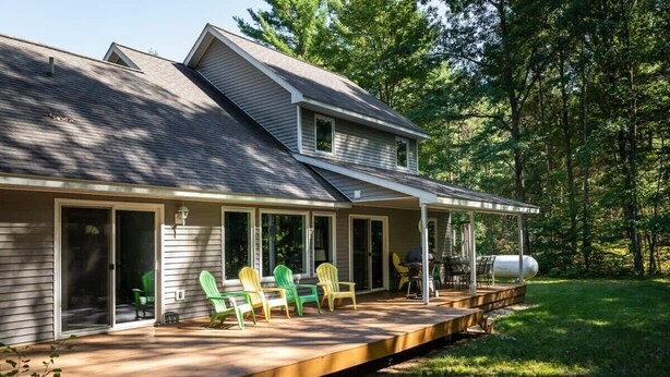 Ein zweigeschossiges Haus mit überdachter Veranda, Schiebetüren und einer Terrasse mit Gartenmöbeln.
