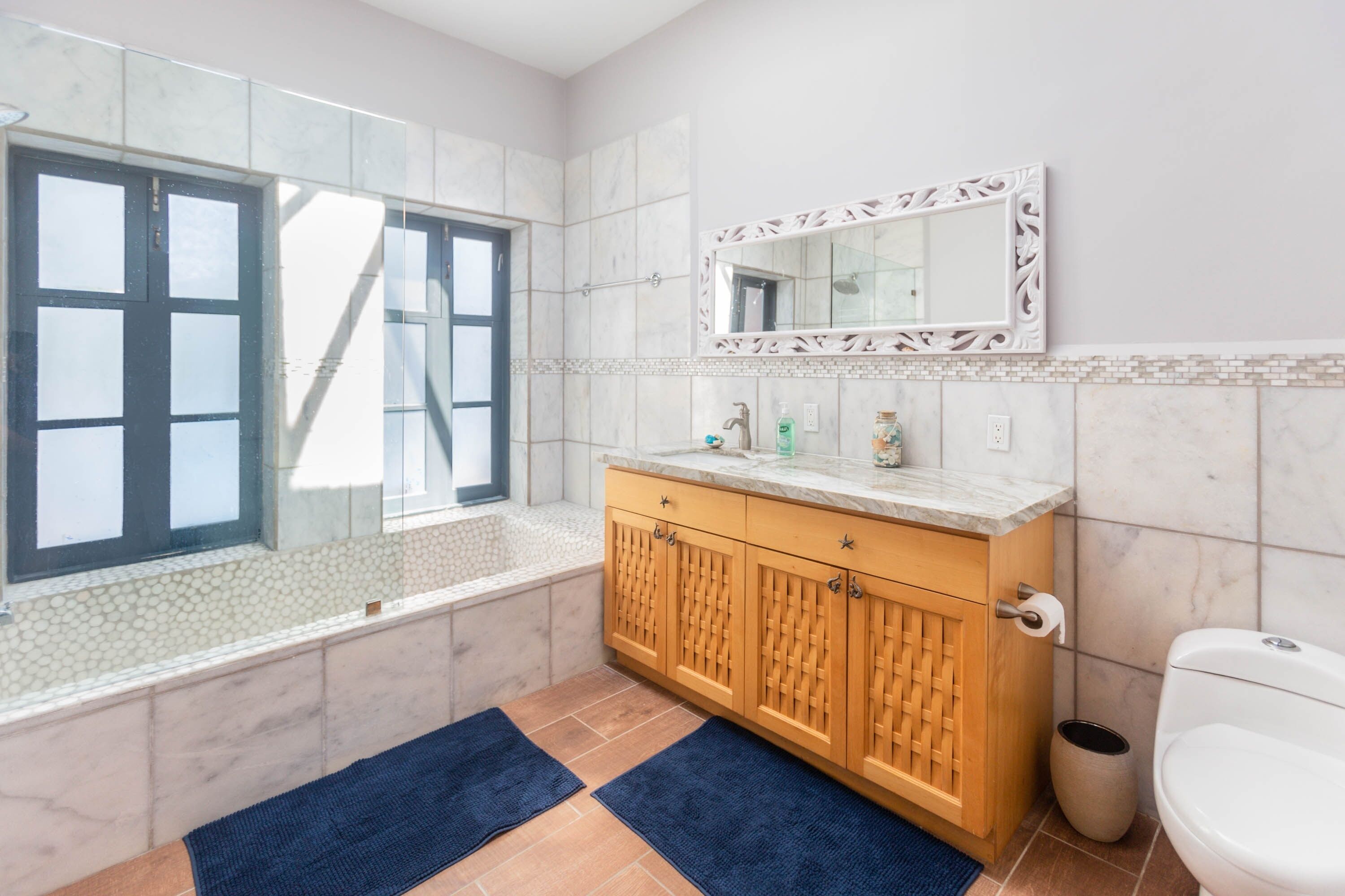 A bathroom with a bathtub, a toilet, a sink with a mirror, and a window.