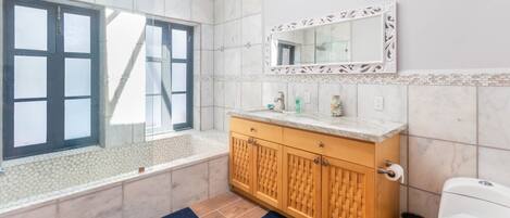 A bathroom with a bathtub, a toilet, a sink with a mirror, and a window.