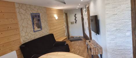 A modern room with a black sofa, wooden panel walls, a stone accent wall, a mounted TV, and a small wooden table.