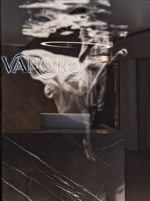 A marble reception desk with a logo and a blurred background. - Vanoro Hotel (Thessaloniki)