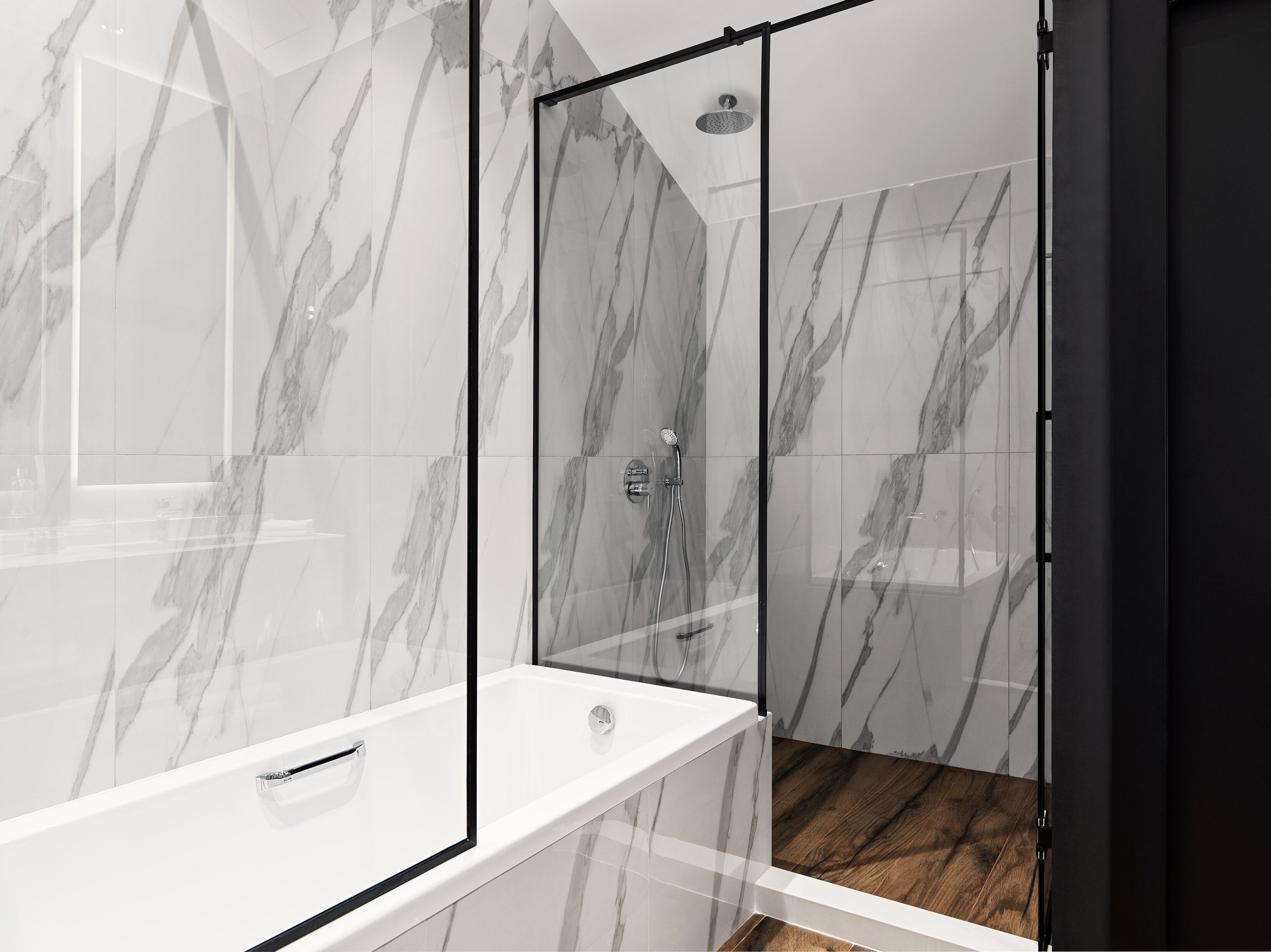 A modern bathroom with a glass-enclosed shower, marble walls, and a wooden floor.