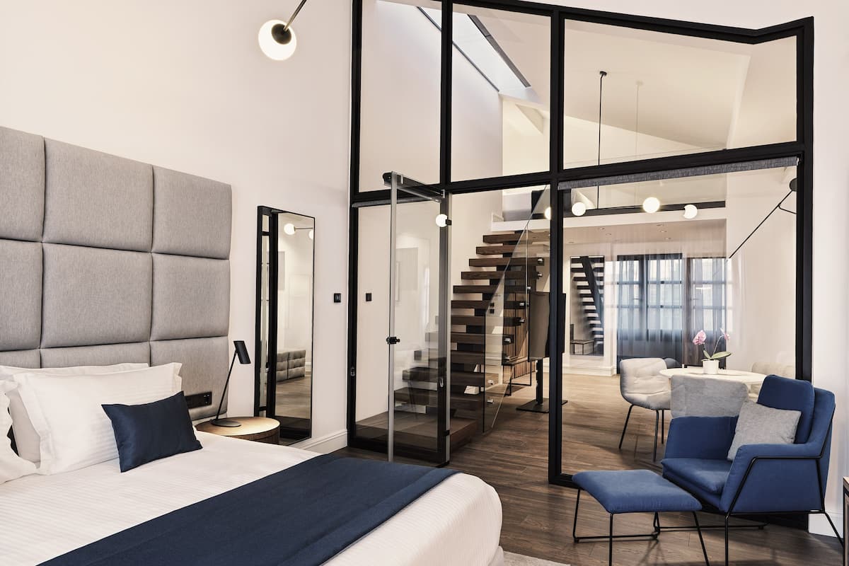 A modern bedroom with a large bed, a glass partition, a staircase, and a seating area.