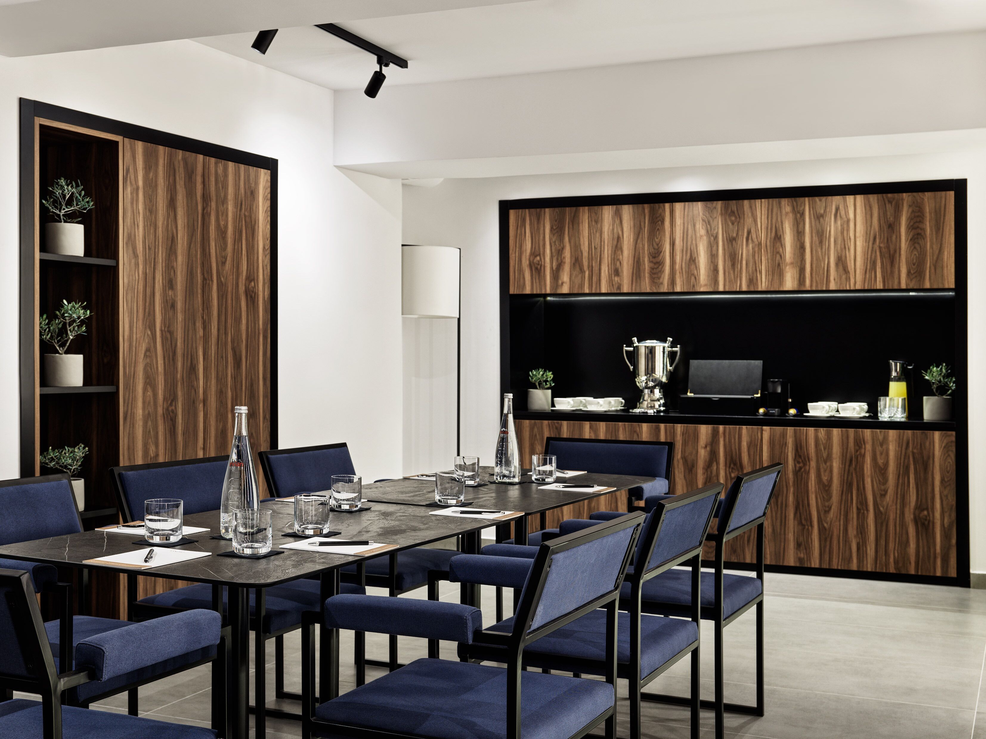 Un espace de salle à manger moderne, avec une longue table, des chaises à revêtement bleu et un mur décoratif en bois.