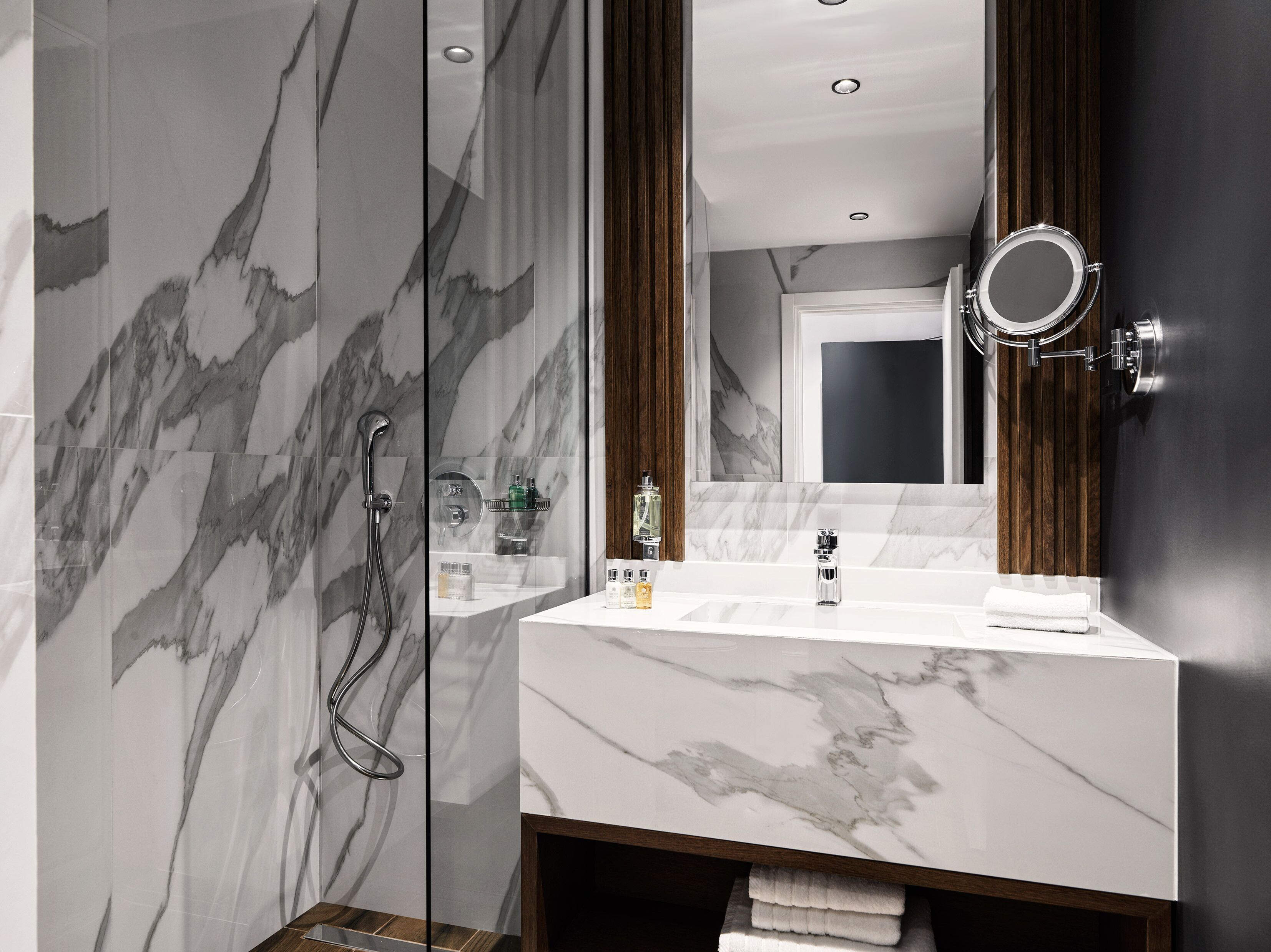 A modern bathroom with a marble vanity, a glass-enclosed shower, and a wooden panel accent.