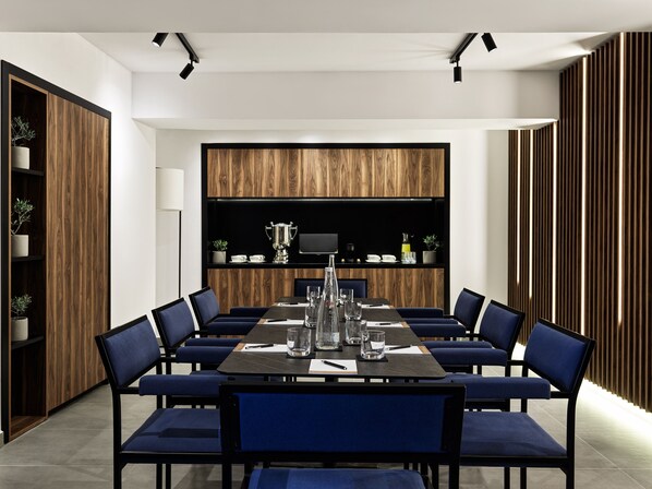 A modern conference room with a long table, blue chairs, and wooden paneling on the walls. - Vanoro Hotel (Thessaloniki)
