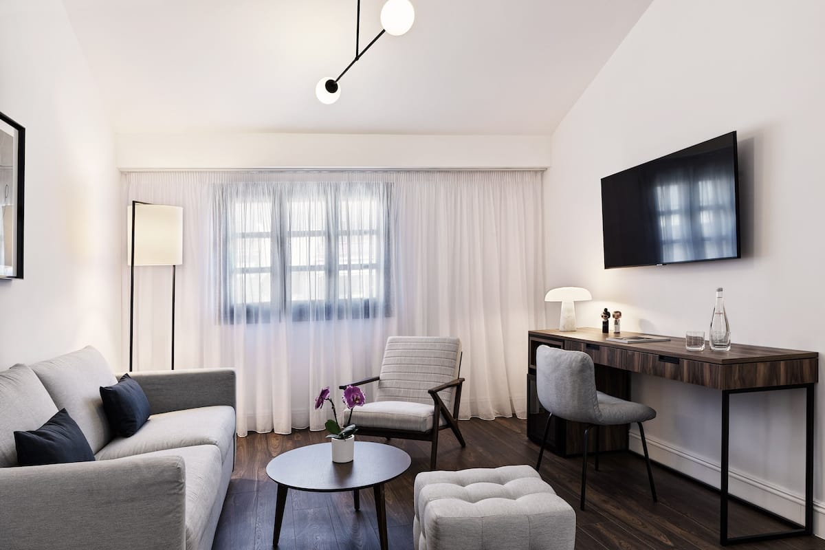 A modern living room with a sofa, armchairs, a coffee table, and a desk with a lamp and a bottle.