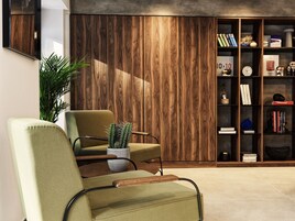 Una sala moderna con un sillón verde, una estantería de madera y una planta de cactus.